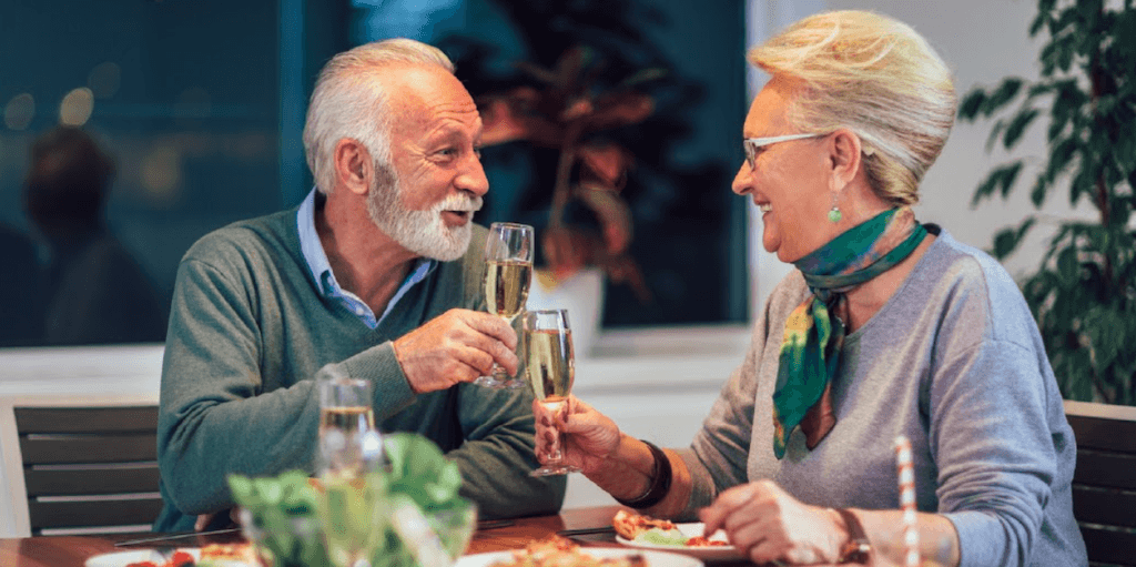 Older, baby boomer couple on a date smiling and toasting with champagne at a dinner table.