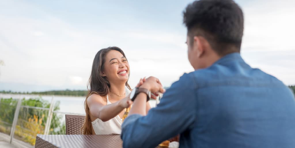 A woman reaches out to hold her date's hand while sitting at a table overlooking a river as a sign she is ready to date again.